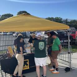 Soccer game attendees talking to IRC staff under yellow tent.